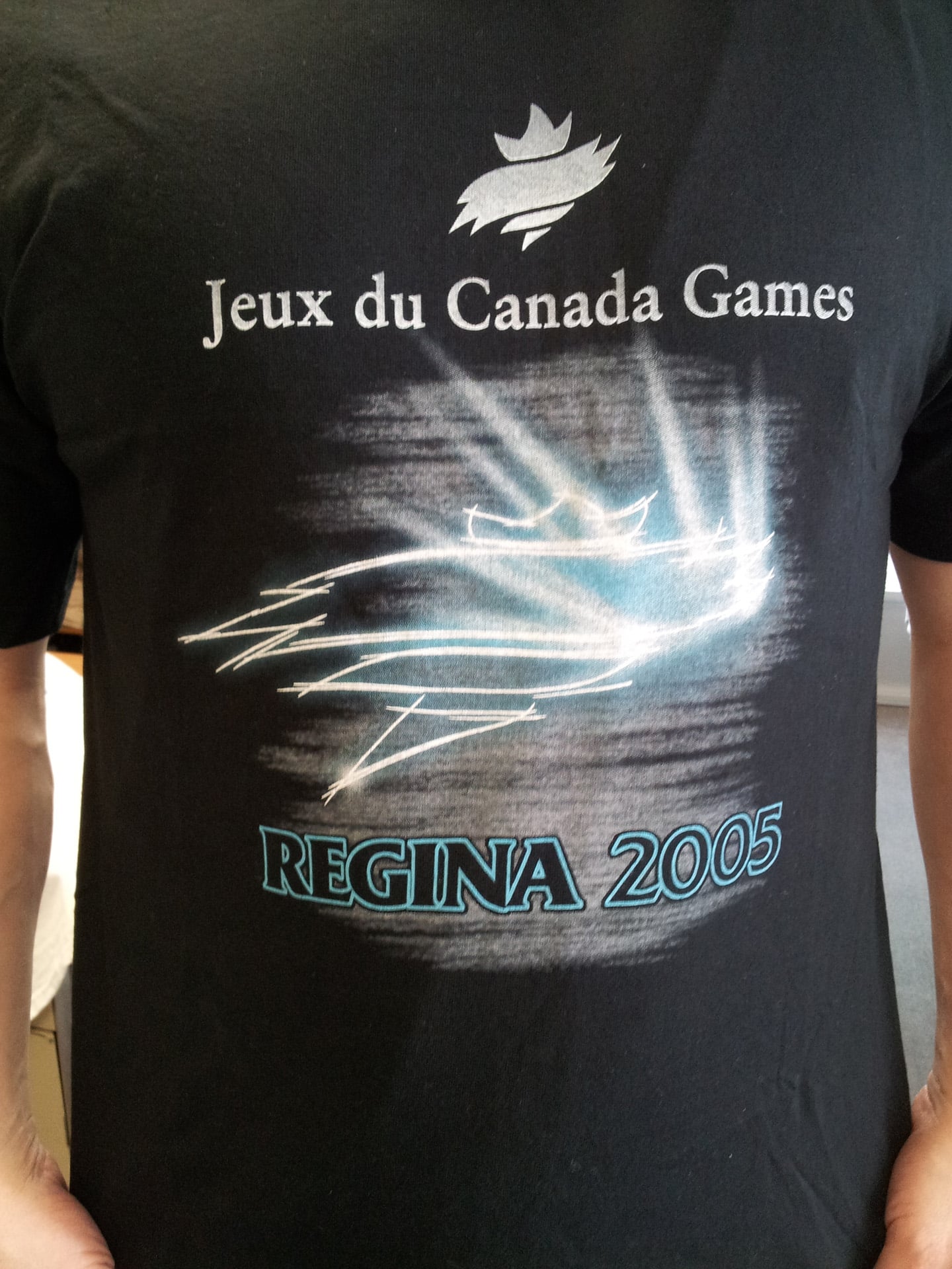 A man wearing a t-shirt that reads "Regina 2005" stands casually, smiling at the camera.
