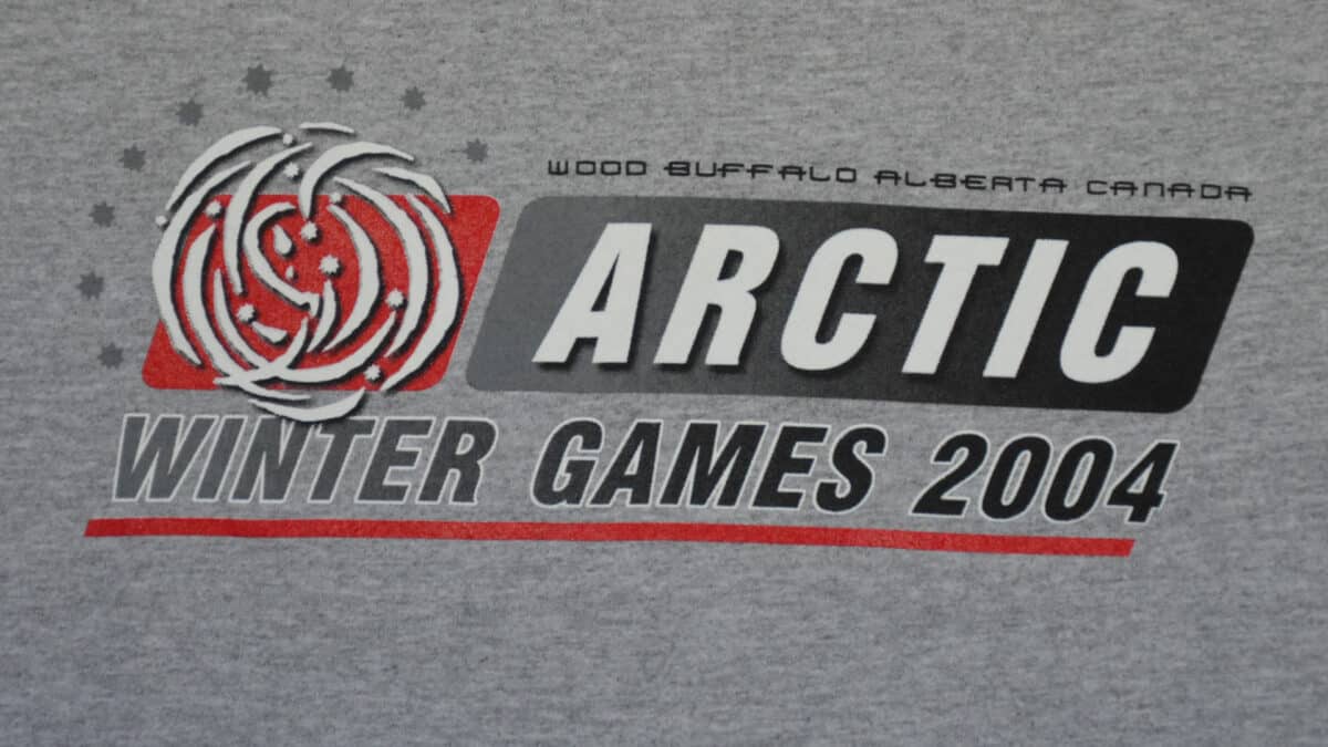 A grey t-shirt featuring the Arctic Winter Games logo prominently displayed on the front.