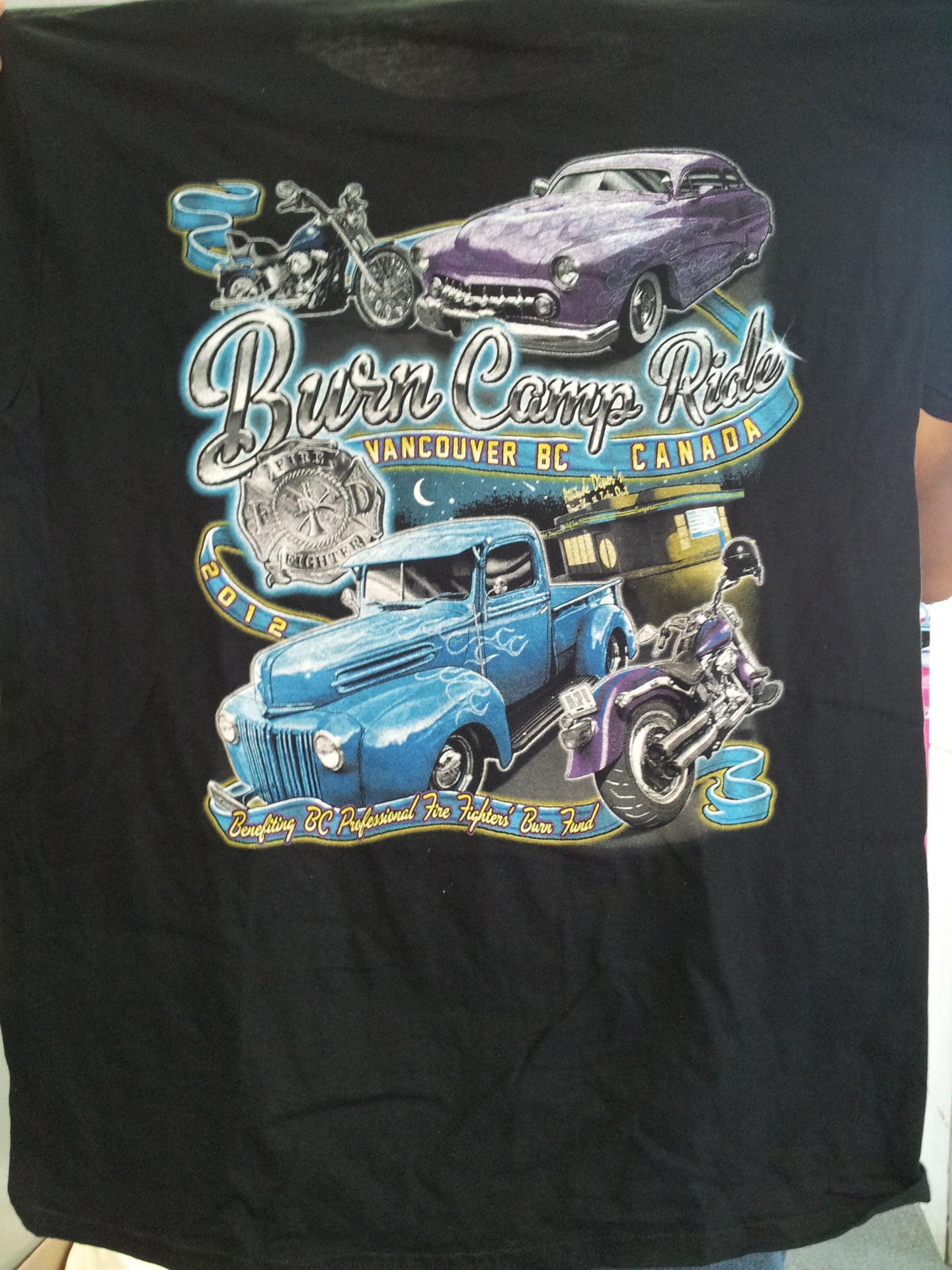 A man displays a shirt featuring an image of a car and a truck.